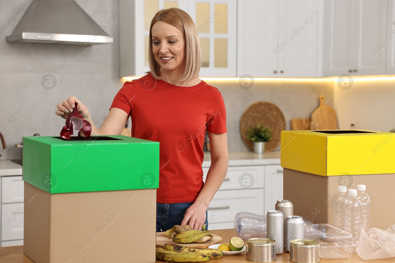 Photo of Smiling woman separating garbage at table in kitchen