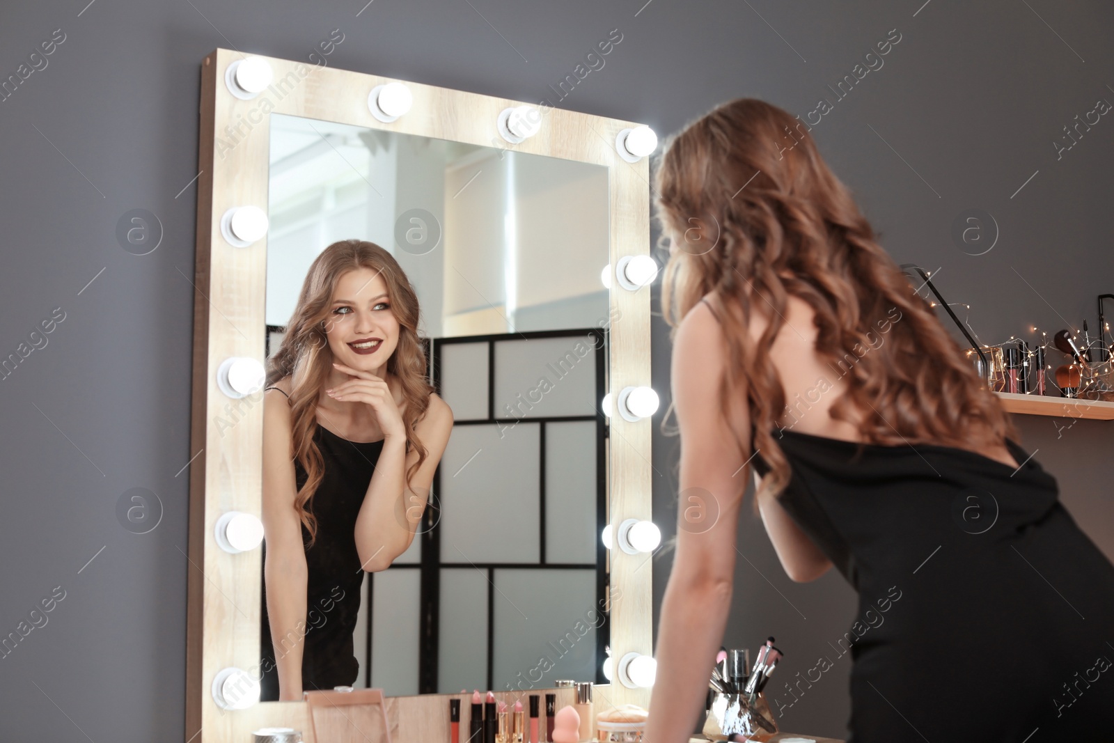 Photo of Young beautiful woman near mirror in makeup room