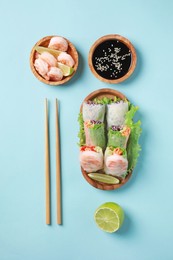 Delicious spring rolls, shrimps, lime, soy sauce and chopsticks on light blue background, flat lay