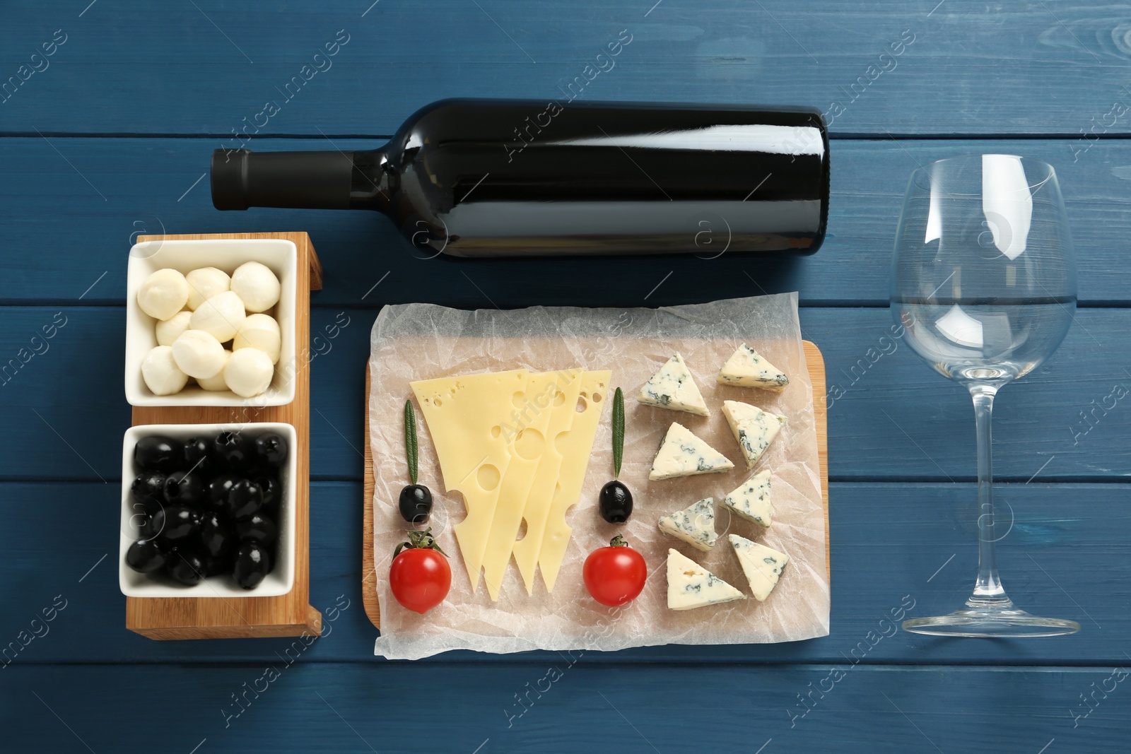 Photo of Tasty red wine and snacks on blue wooden table, flat lay