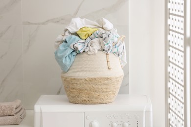 Photo of Wicker basket with dirty clothes on washing machine in bathroom