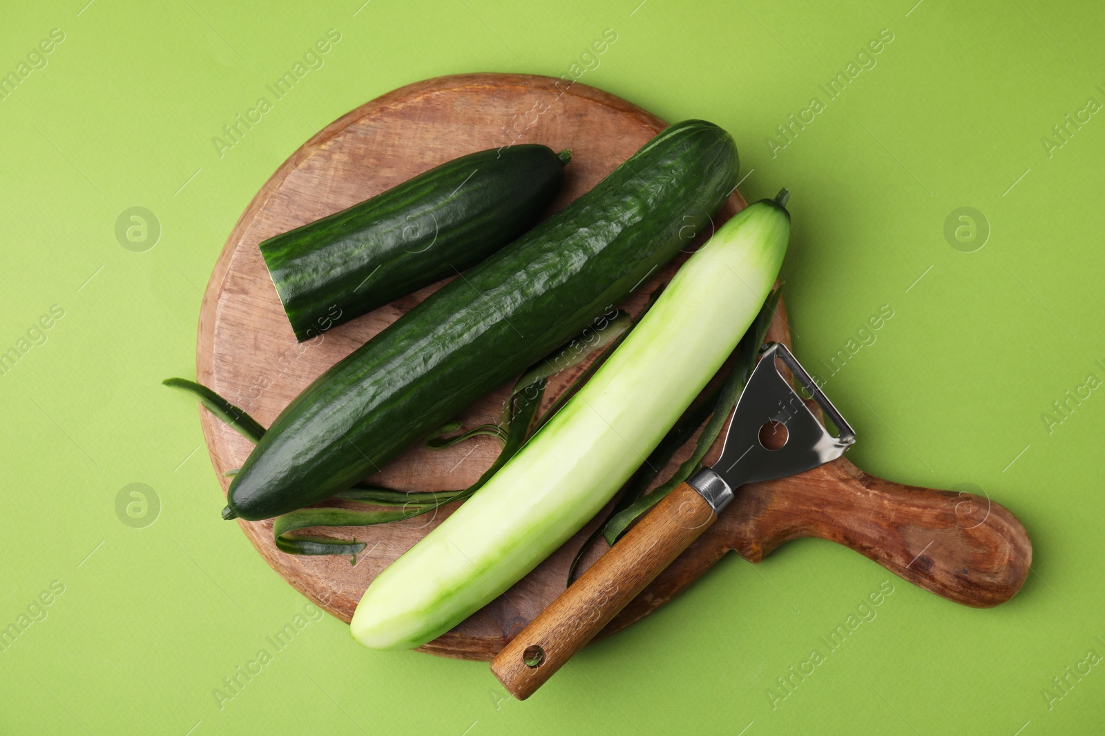 Photo of Fresh cucumbers and peeler on green background, top view