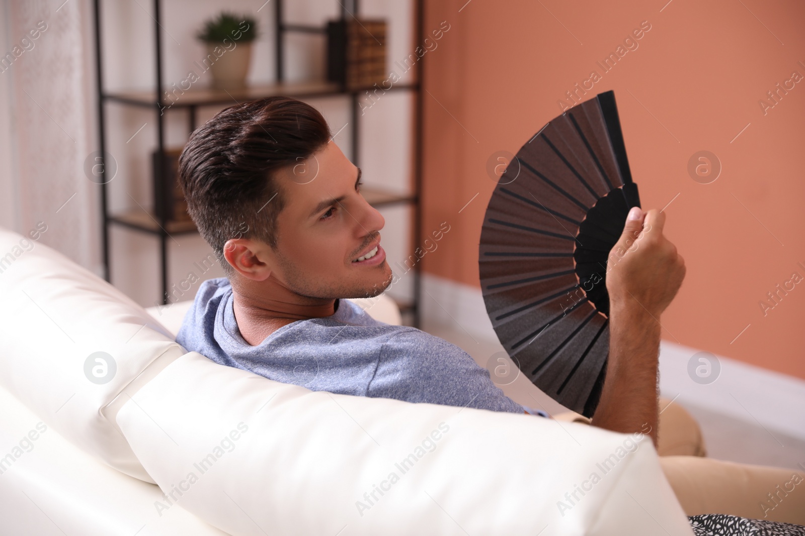 Photo of Man with hand fan sitting on sofa. Summer season