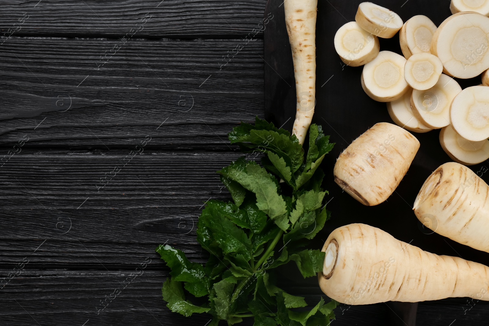 Photo of Whole and cut parsnips on black wooden table, flat lay. Space for text