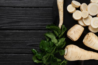 Photo of Whole and cut parsnips on black wooden table, flat lay. Space for text