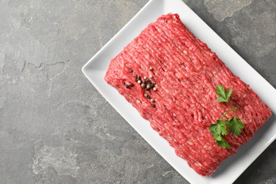 Photo of Raw ground meat, parsley and peppercorns on grey table, top view. Space for text