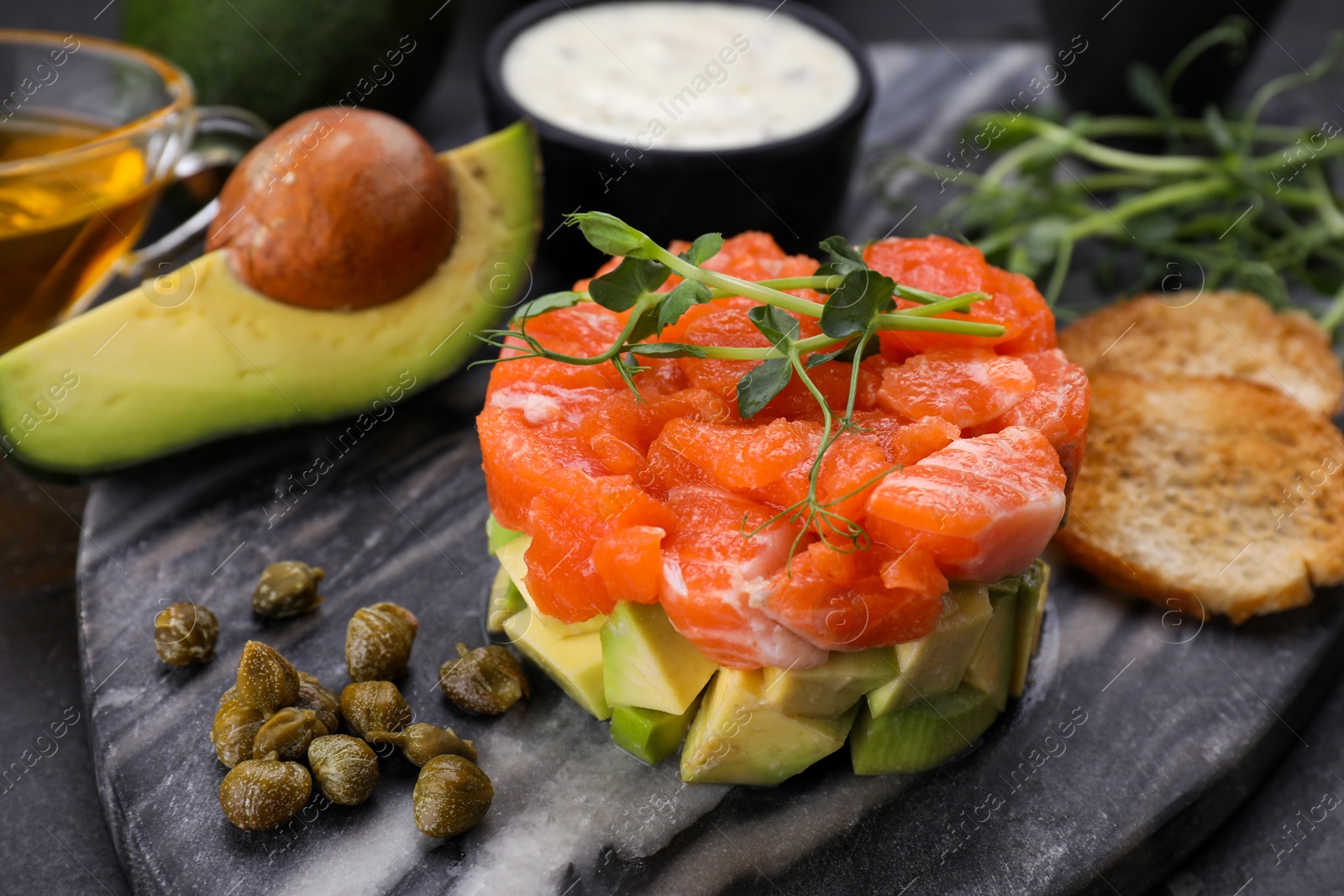 Photo of Delicious salmon tartare served with avocado and croutons on dark table, closeup