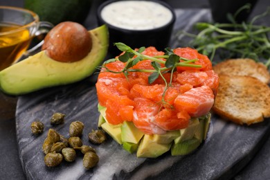 Photo of Delicious salmon tartare served with avocado and croutons on dark table, closeup