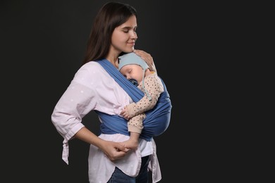 Photo of Mother holding her child in sling (baby carrier) on black background. Space for text