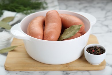 Bowl of delicious sausages, dill, bay leaf, pepper and salt on white marble table