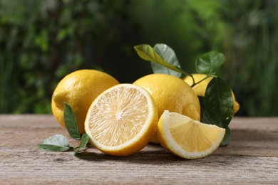 Photo of Fresh lemons and green leaves on wooden table outdoors, closeup