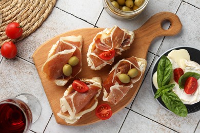 Photo of Tasty sandwiches with cured ham, tomatoes and olives on tiled table, flat lay