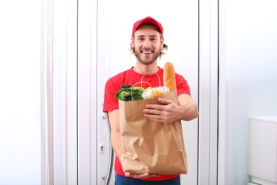 Photo of Delivery man holding paper bag with food products indoors