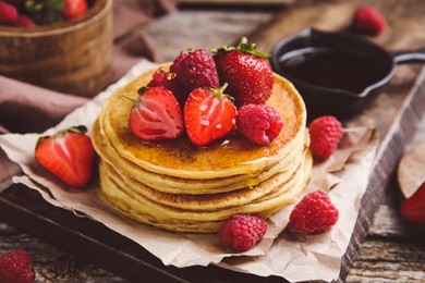 Tasty pancakes with fresh berries and honey on wooden board, closeup