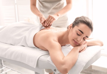 Young woman having body scrubbing procedure with sea salt in spa salon