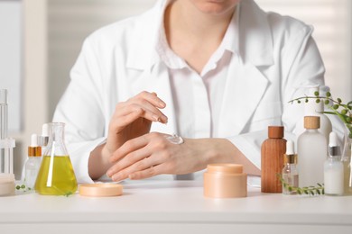 Photo of Dermatologist applying cream onto hand at white table indoors, closeup. Testing cosmetic product