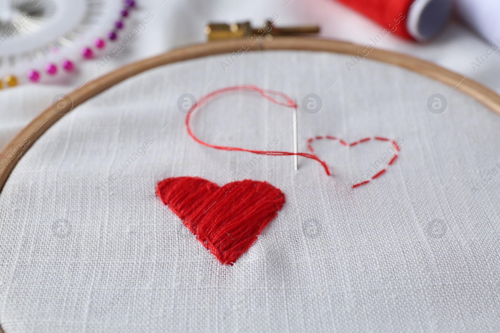 Photo of Embroidered red hearts and needle on white cloth, closeup