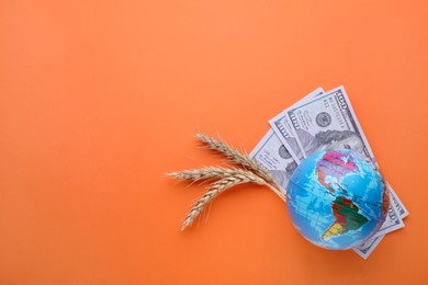 Import and export concept. Globe, ears of wheat and banknotes on orange background, flat lay. Space for text
