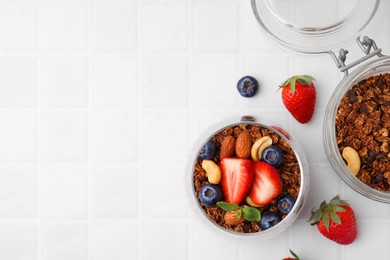 Photo of Tasty granola with berries, nuts and mint in glass on white tiled table, flat lay. Space for text