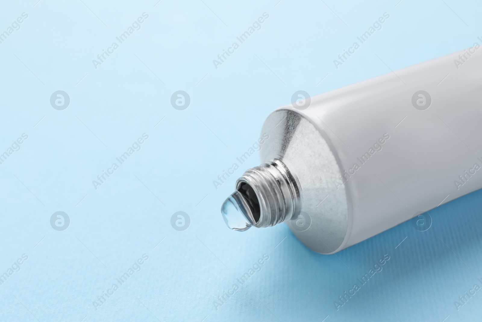 Photo of Open tube of ointment on light blue background, closeup. Space for text