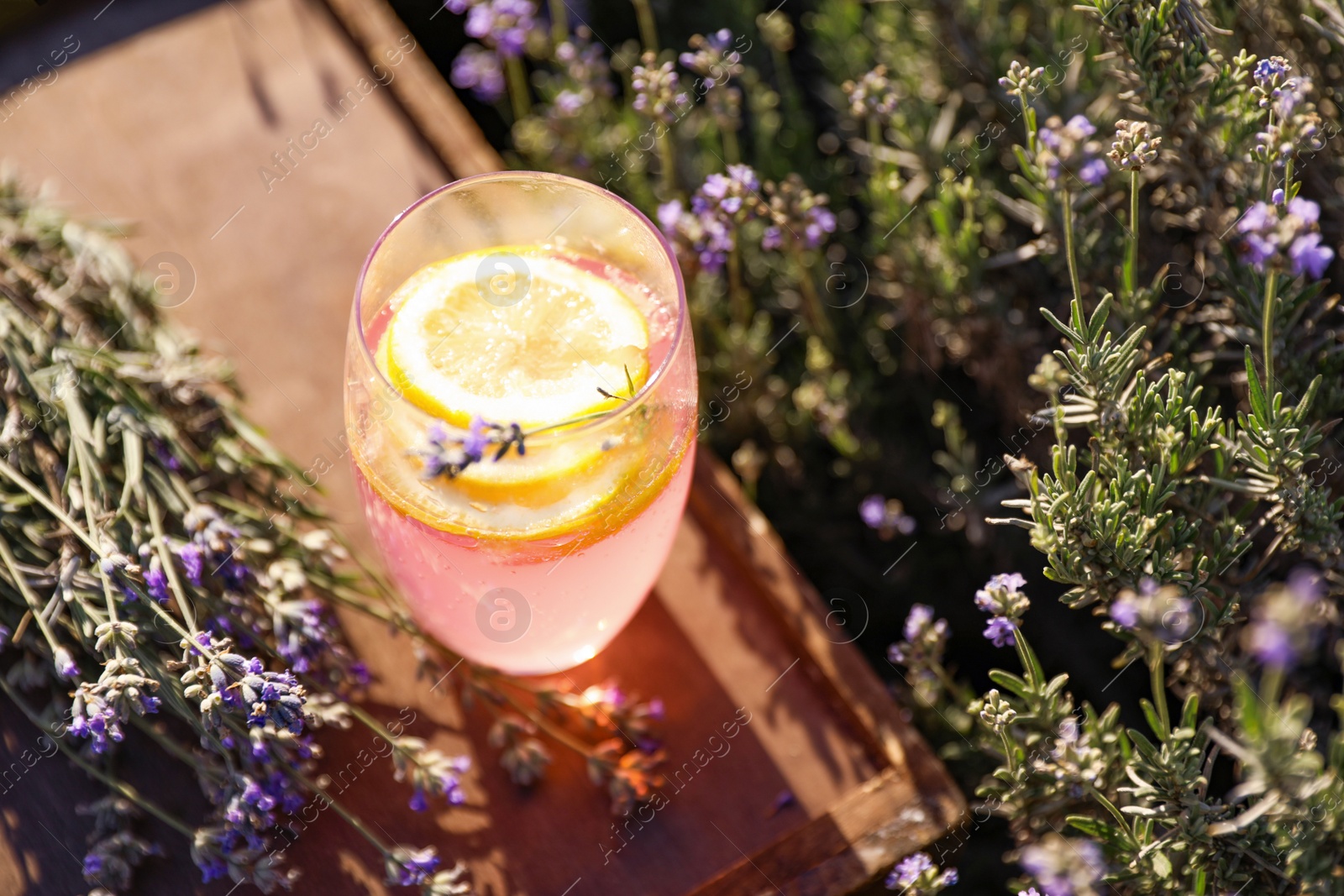 Photo of Glass of fresh lemonade on wooden tray in lavender field