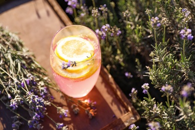 Glass of fresh lemonade on wooden tray in lavender field