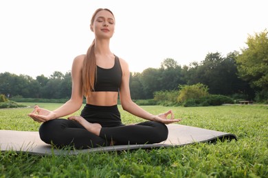 Beautiful young woman practicing Padmasana on yoga mat outdoors. Lotus pose