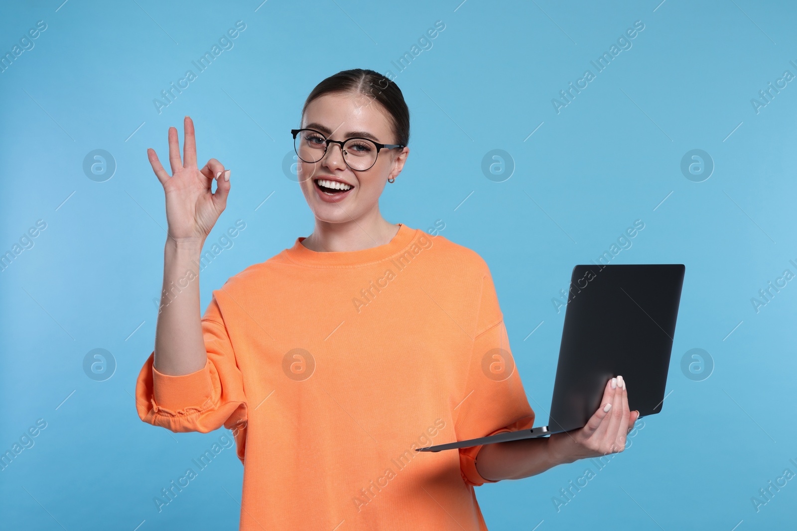 Photo of Happy woman with laptop showing okay gesture on light blue background