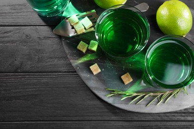 Photo of Absinthe in glasses, rosemary, brown sugar and lime on black wooden table, top view with space for text. Alcoholic drink