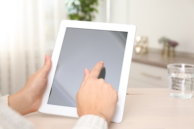 Photo of Woman using tablet at table indoors, closeup