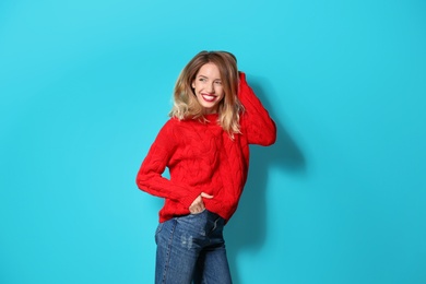 Beautiful young woman in warm sweater on color background