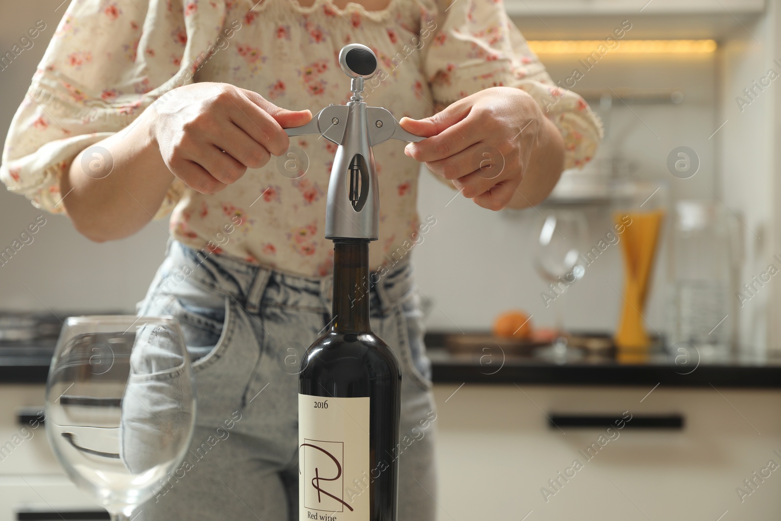 Photo of Woman opening wine bottle with corkscrew in kitchen, closeup