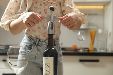 Woman opening wine bottle with corkscrew in kitchen, closeup