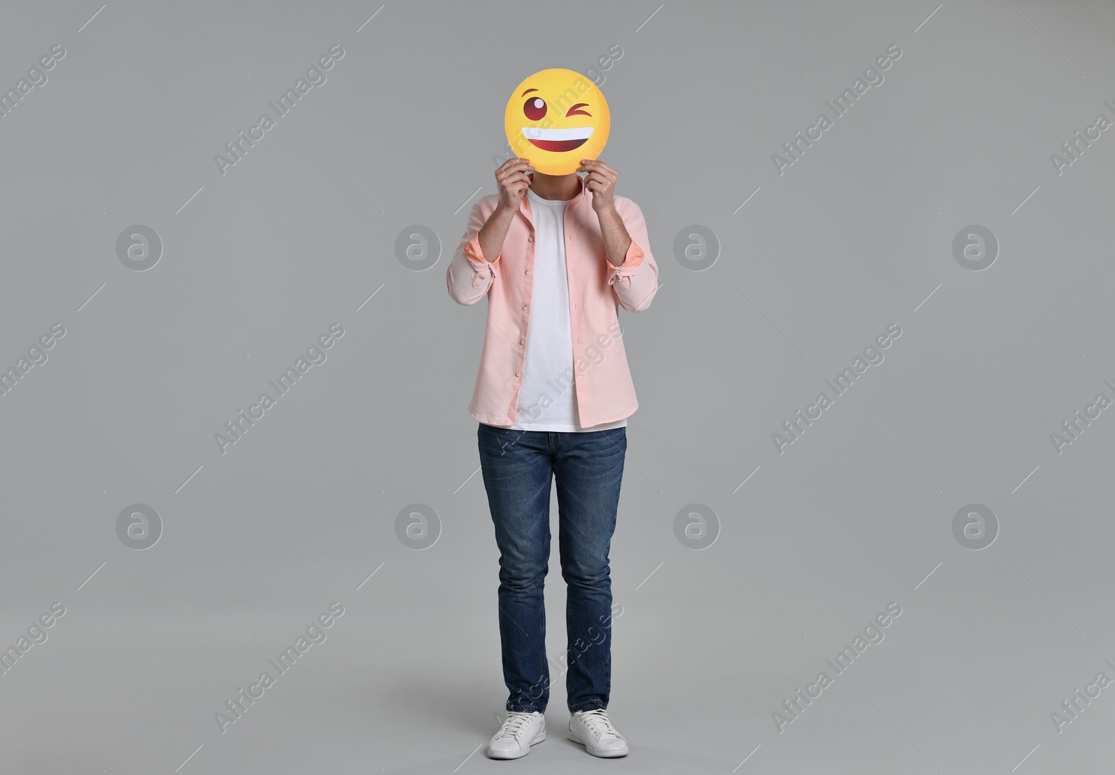 Photo of Man covering face with happy winking emoticon on grey background