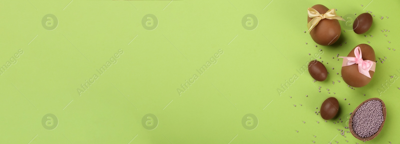 Image of Sweet chocolate eggs on light green background, flat lay with space for text. Banner design