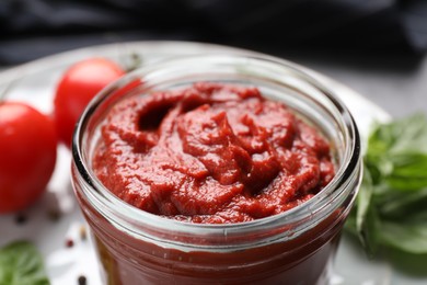 Photo of Jar of tasty tomato paste on table, closeup