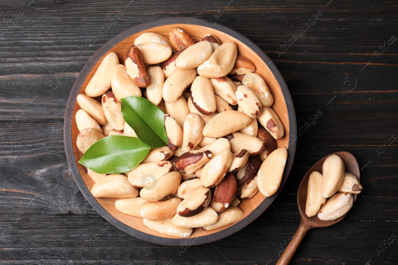 Photo of Bowl and spoon with Brazil nuts on wooden background, top view