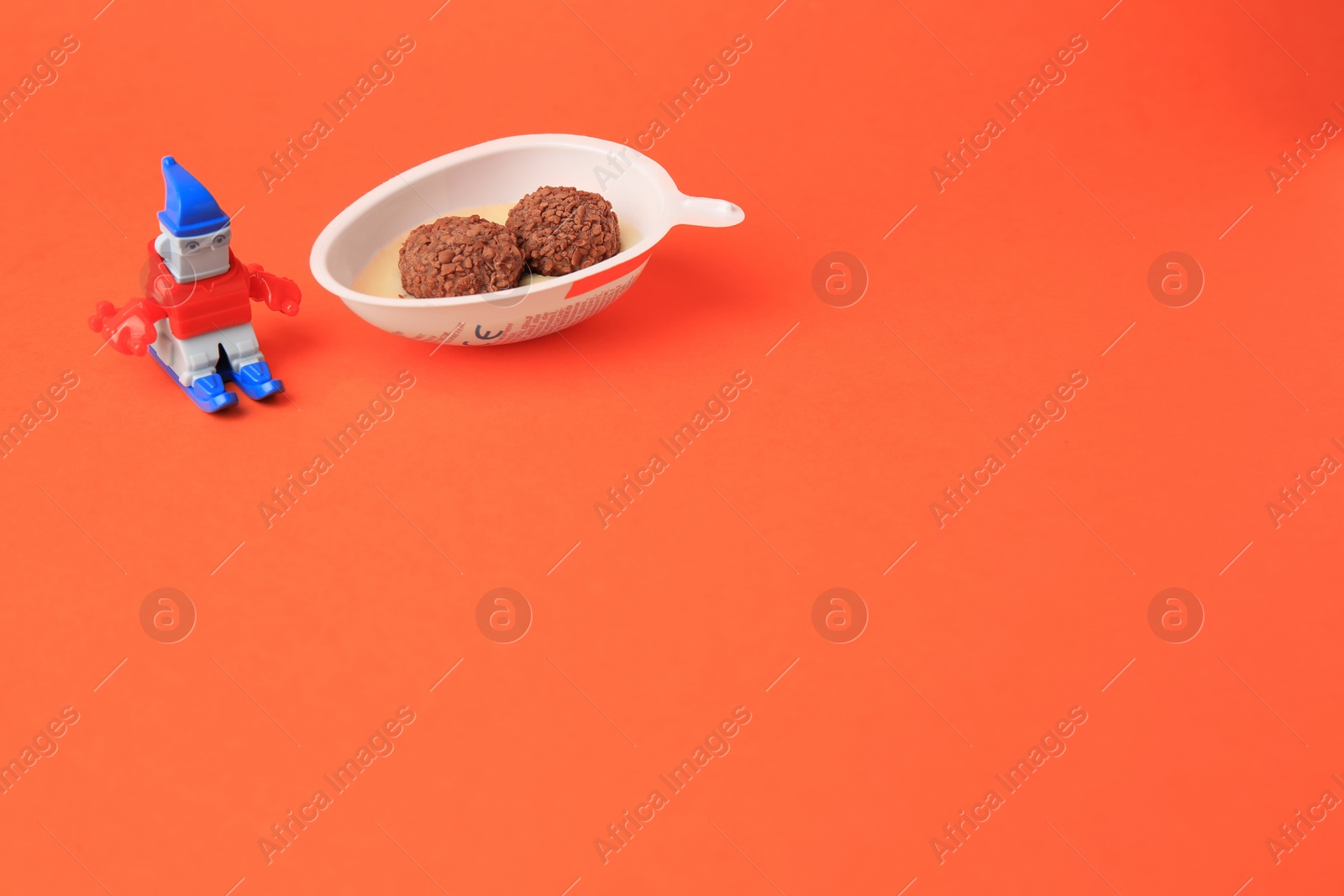 Photo of Slynchev Bryag, Bulgaria - May 25, 2023: Half of Kinder Joy Egg with sweet candies and toy on orange background, space for text