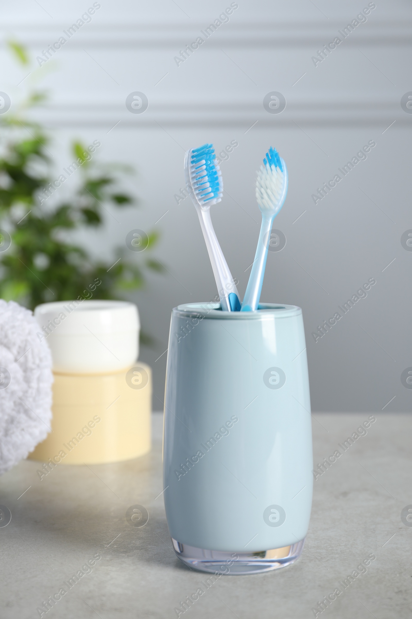 Photo of Plastic toothbrushes in holder, towel and cosmetic products on light grey table