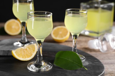 Photo of Tasty limoncello liqueur, lemon and green leaf on table, closeup