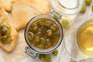 Photo of Jar of delicious gooseberry jam, tea and bread on table, flat lay