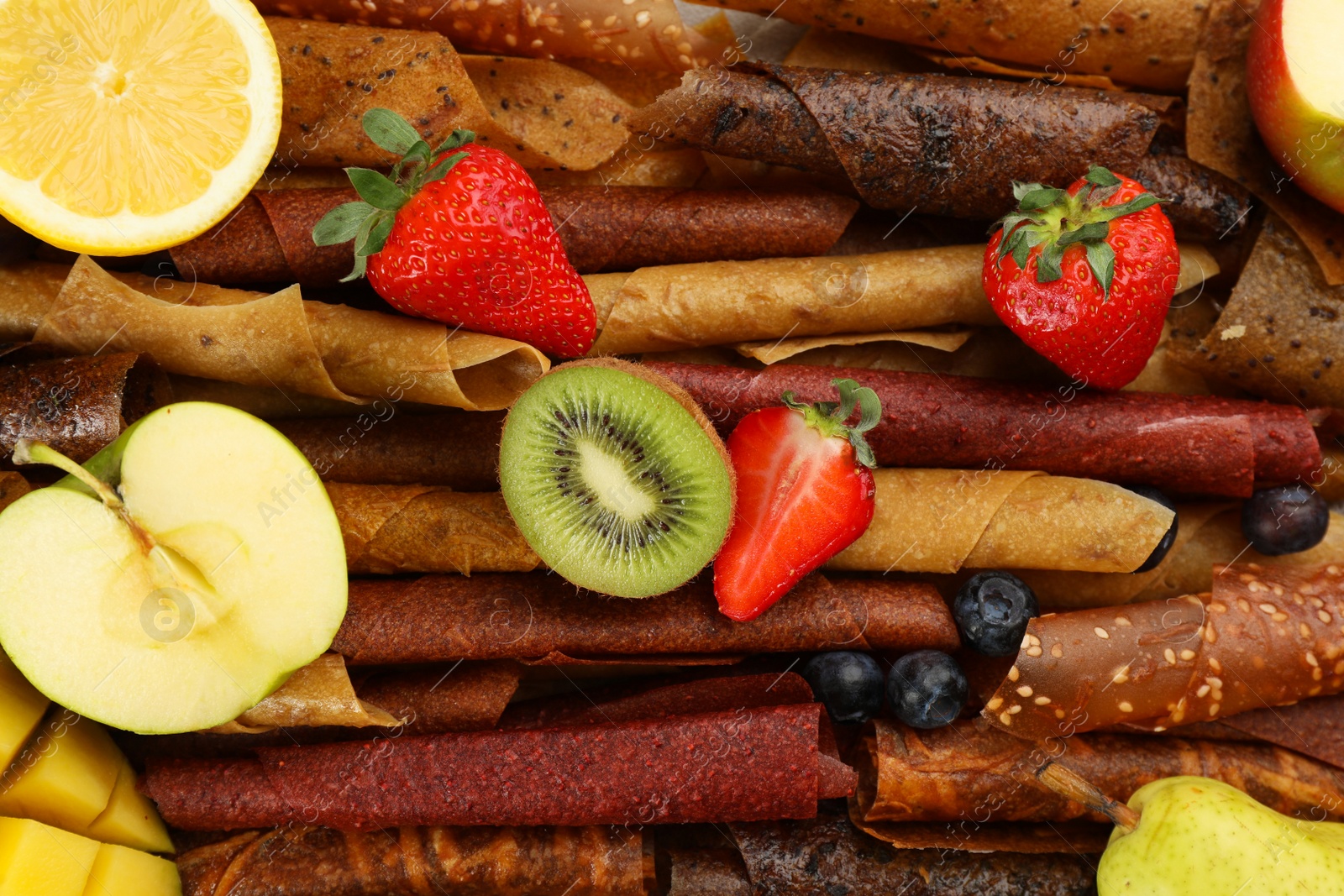 Photo of Delicious fruit leather rolls with ingredients as background, top view