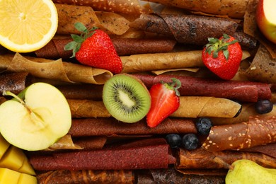 Delicious fruit leather rolls with ingredients as background, top view