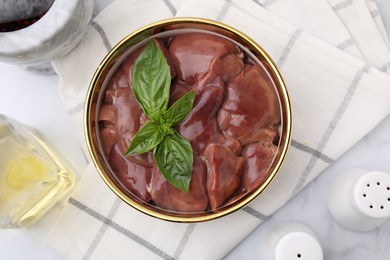 Photo of Bowl with raw chicken liver and basil on white marble table, flat lay