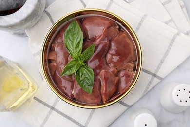 Bowl with raw chicken liver and basil on white marble table, flat lay