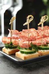 Photo of Tasty canapes with salami, cucumber and cream cheese on grey table, closeup