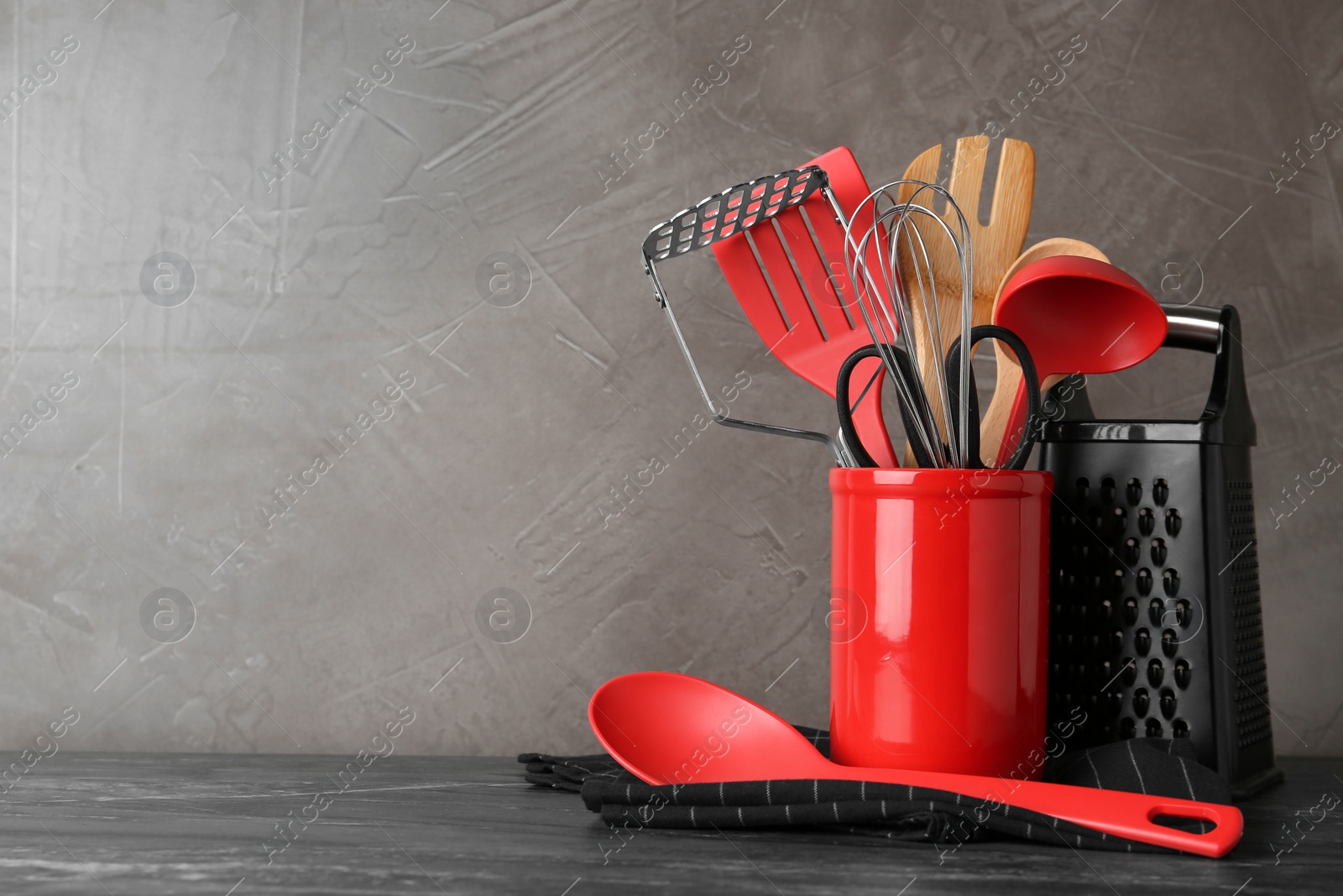 Photo of Holder with kitchen utensils on grey table against grey stone background. Space for text