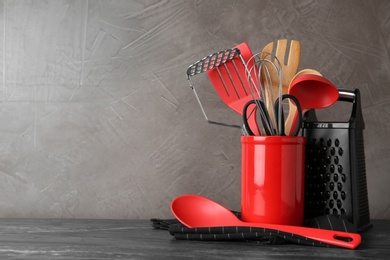 Photo of Holder with kitchen utensils on grey table against grey stone background. Space for text