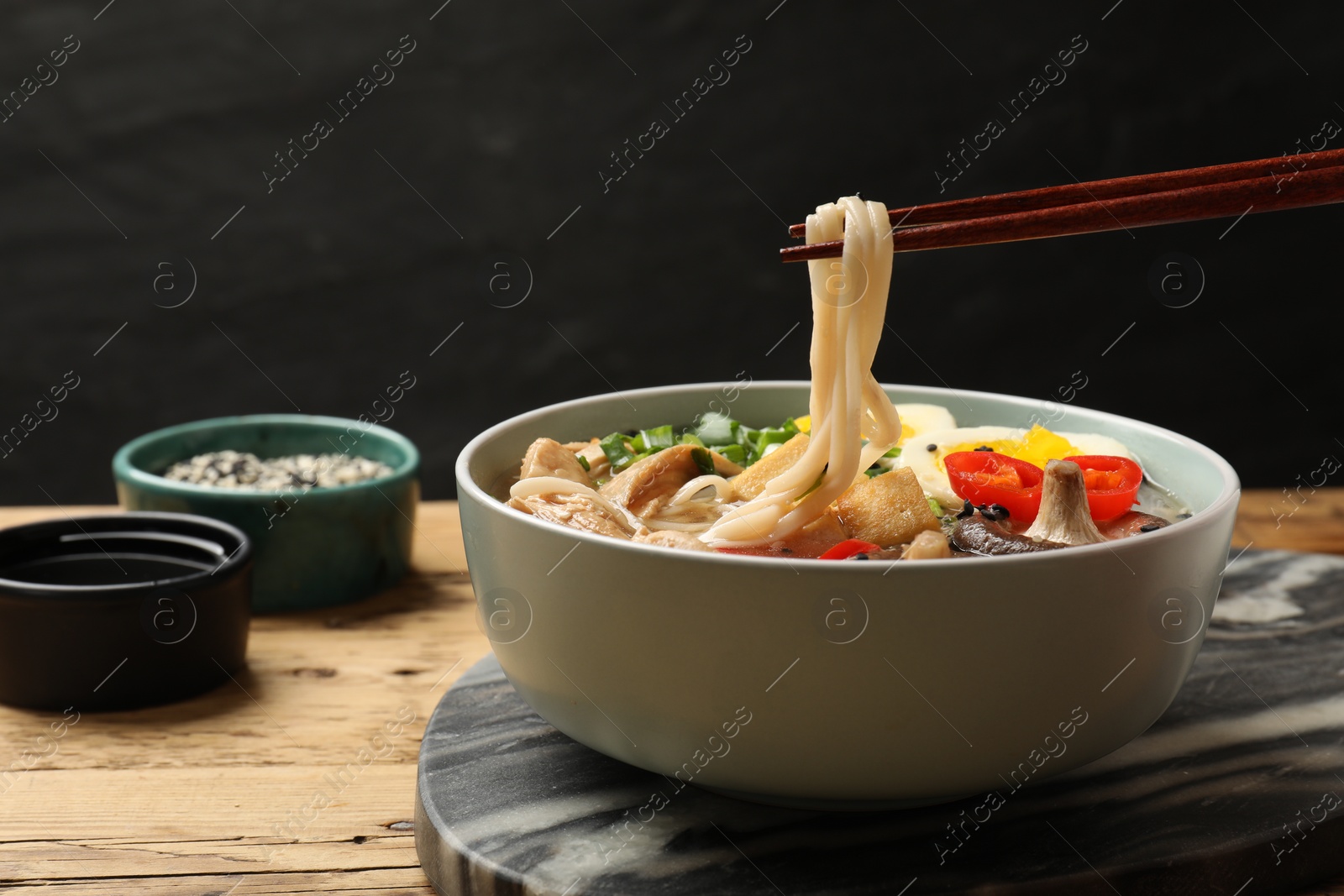 Photo of Eating delicious ramen with chopsticks on wooden table, closeup. Noodle soup