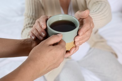 Photo of Caregiver giving drink to elderly woman at home, closeup